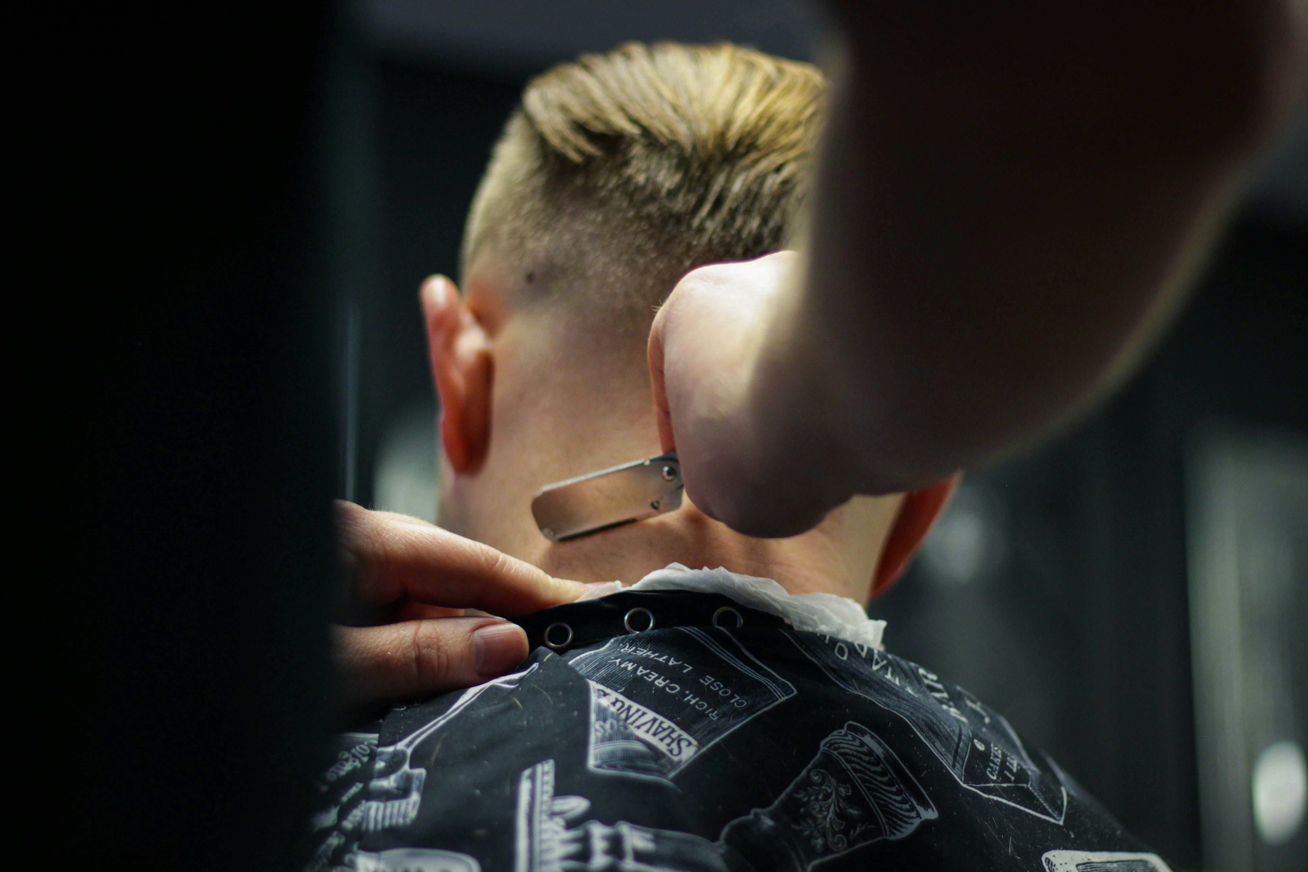 Person mit hellem Haar bekommt Nackenrasur im Friseursalon, entspannt, Fokus auf Rasiermesser.