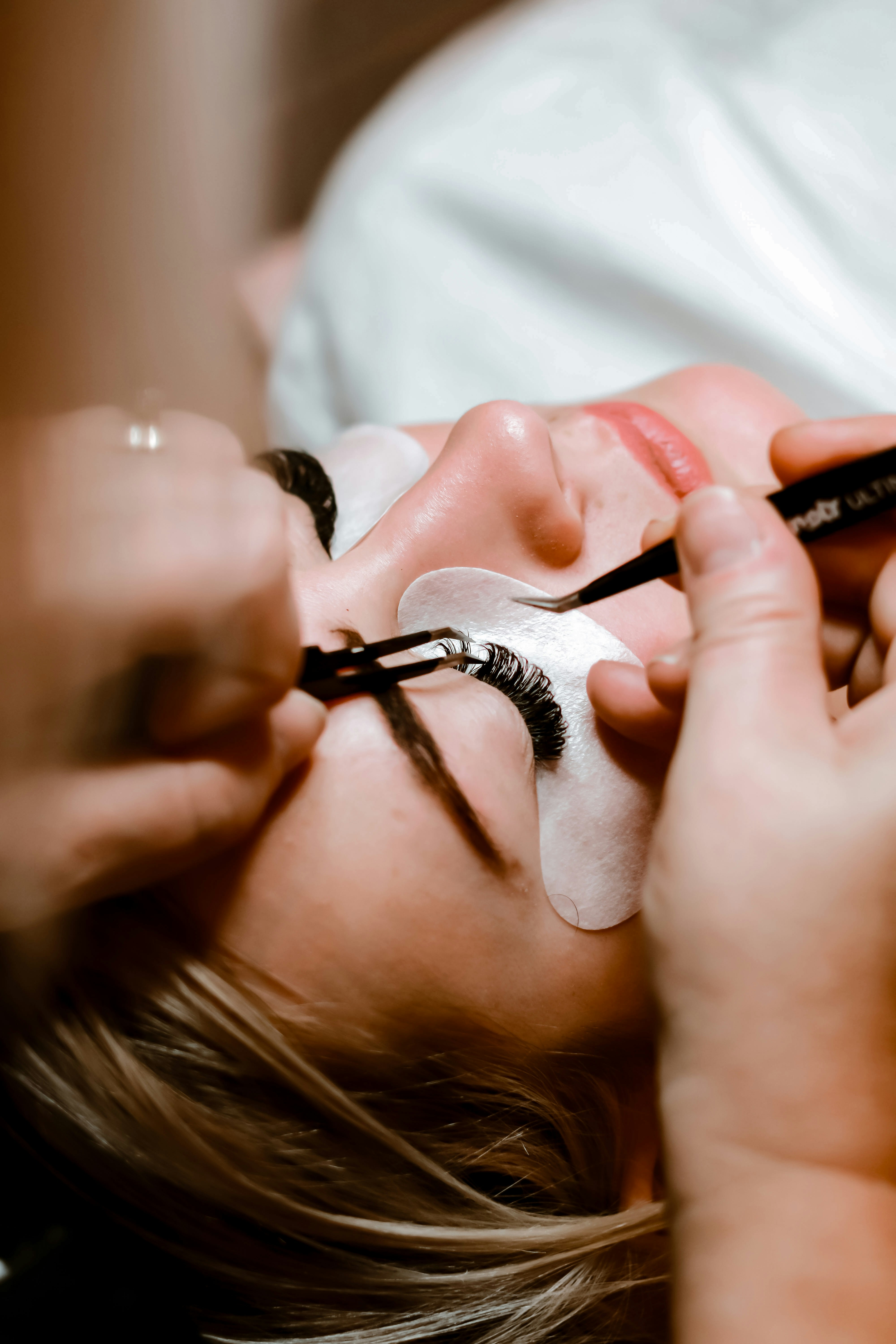 Eine Person bekommt Wimpernextensions, entspannt liegend, mit geschlossenen Augen, blonde Haare.